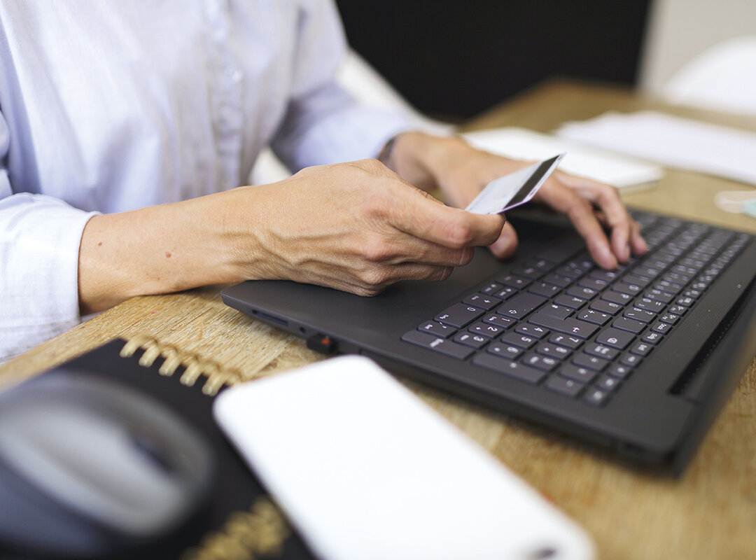Hände vor einem Laptop, die eine Kreditkarte halten.