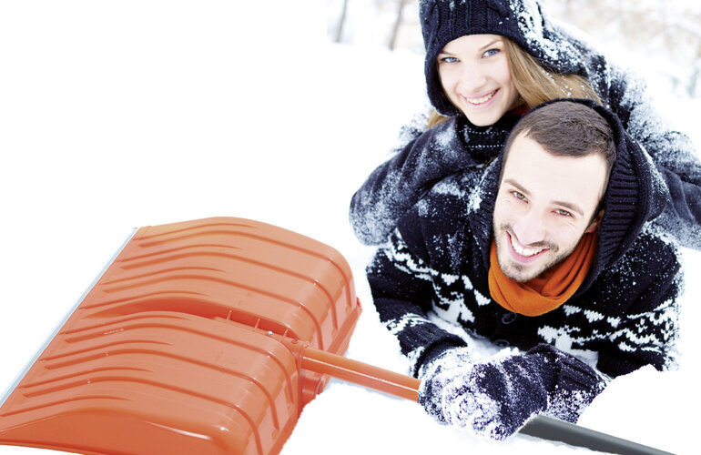 2 Menschen, die mit einer Schneeschaufel im Schnee liegen.