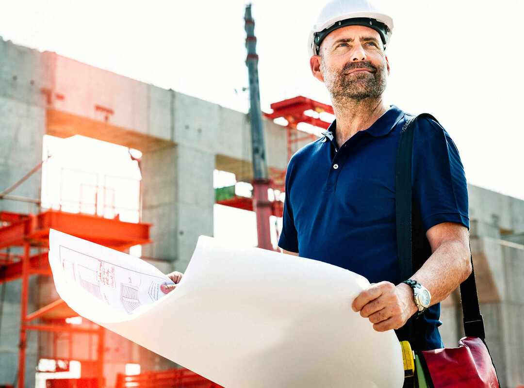 Ein Mann mit Helm, der auf einer Baustelle einen Bauplan hält.