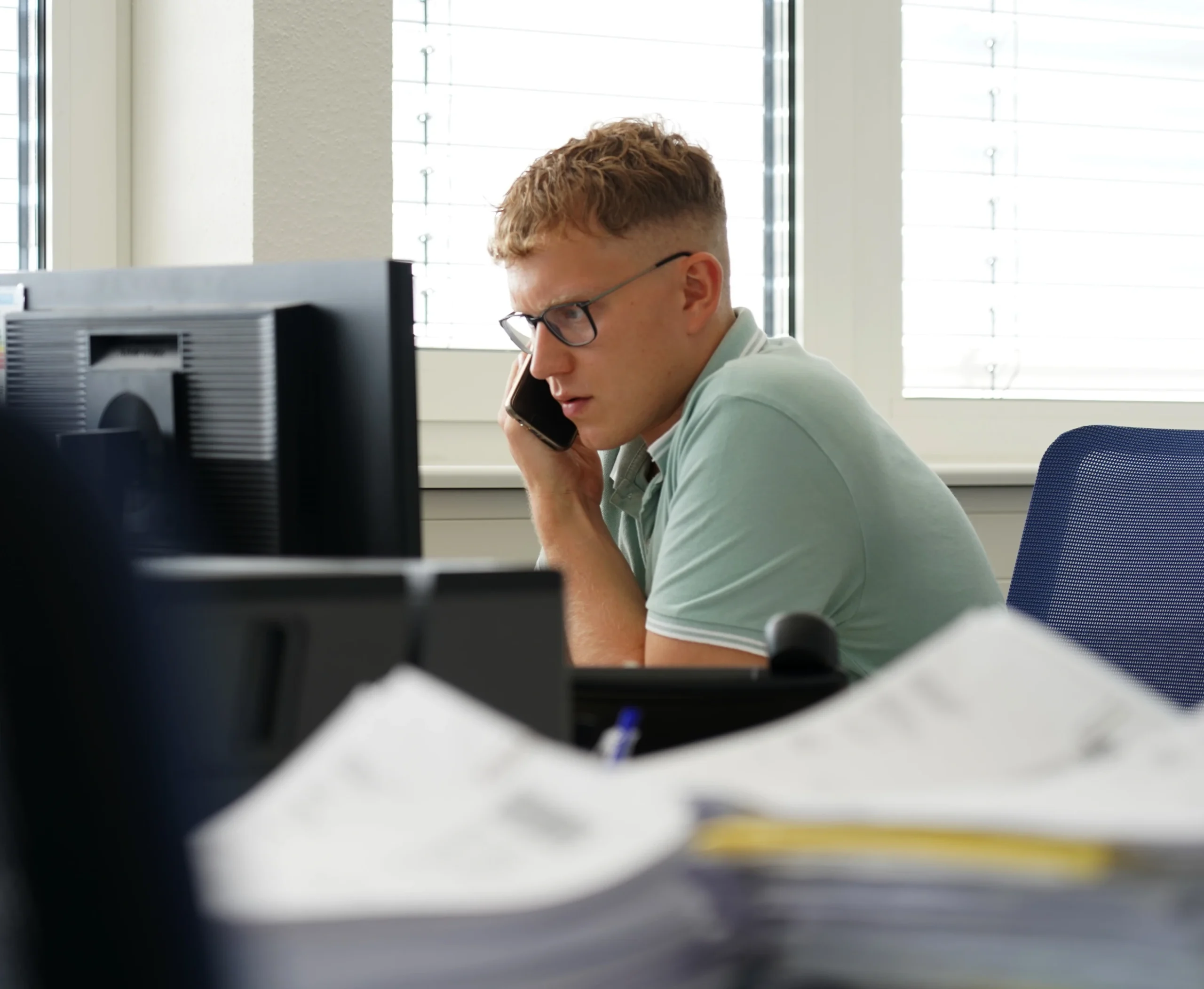 Junger Mann sitzt vor einem Monitor mit Telefon in der Hand