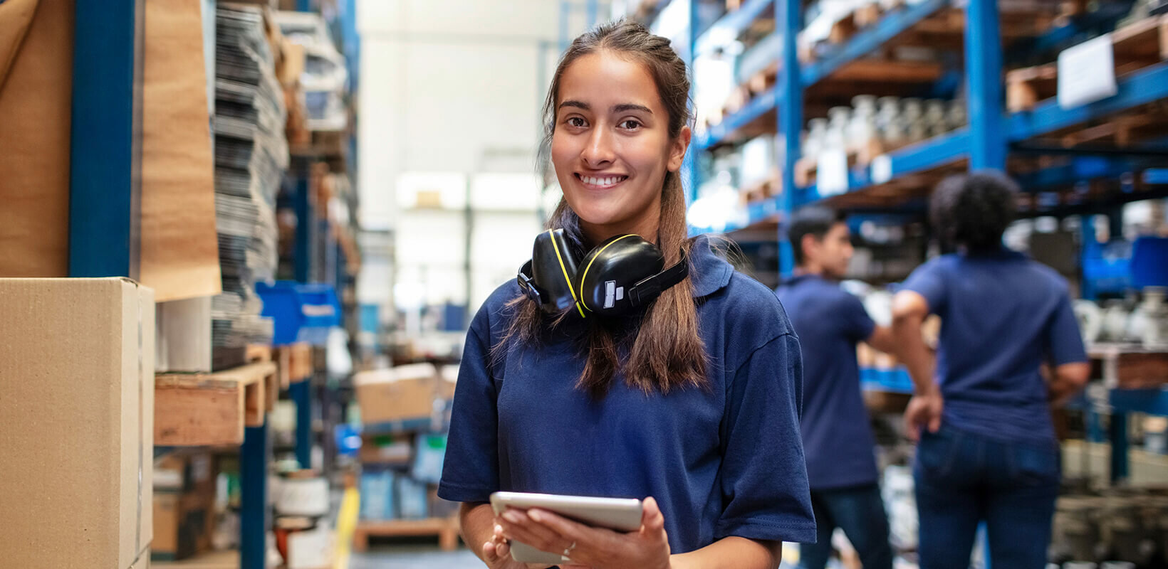 Frau guckt lächelnd in die Kamera. SIe befindet sich in einem Großraumlager