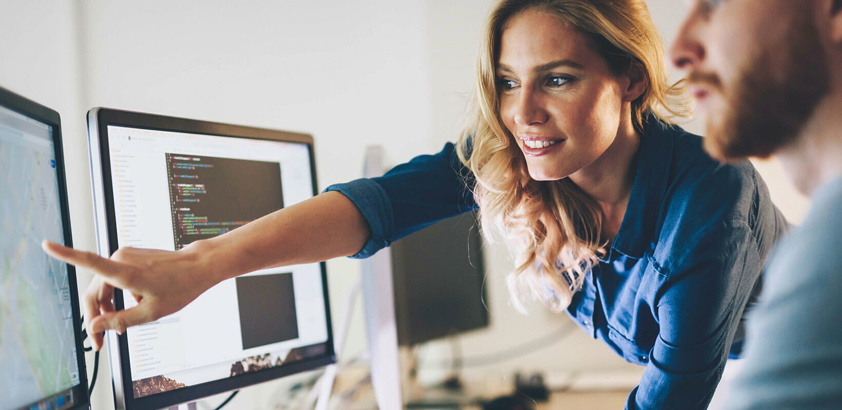 Zwei Personen arbeiten gemeinsam an Computern, eine zeigt auf den Bildschirm.