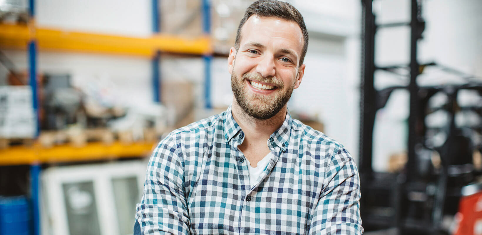 Lächelnder Mann mit kariertem Hemd in Werkstattumgebung.