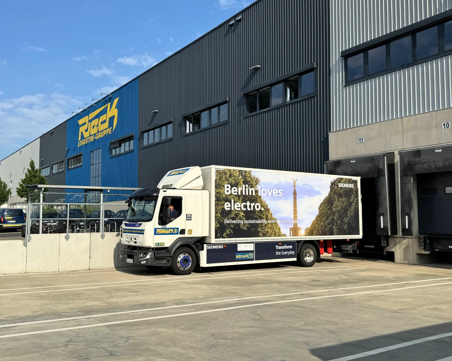 LKW mit Werbebeschriftung vor Lagerhalle mit Roack-Logo bei klarem Himmel.