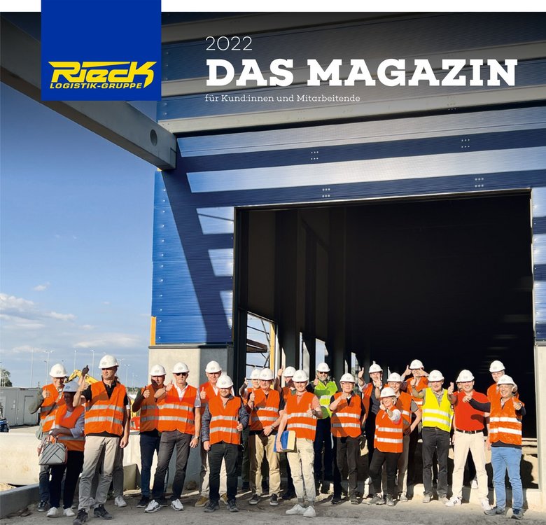 Gruppenfoto von Personen mit Schutzhelmen und Warnwesten vor einem großen Industriegebäude.