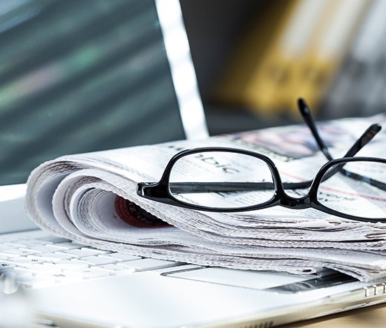Gefaltete Zeitung mit schwarzer Brille auf Laptop-Tastatur.