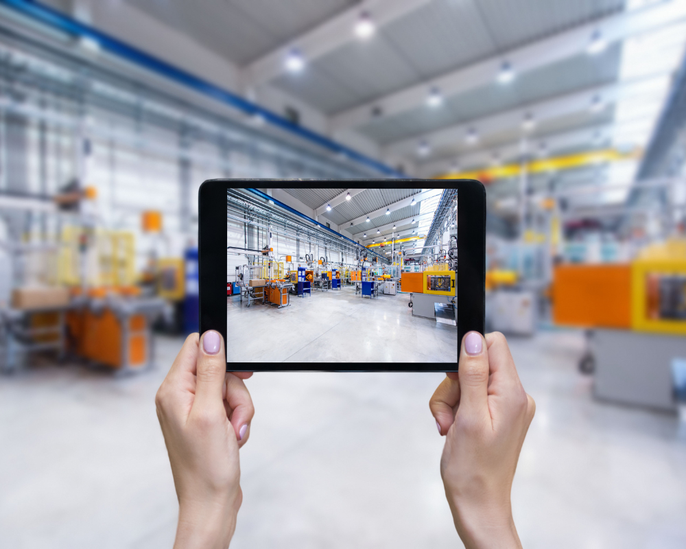 Person hält Tablet, das eine Aufnahme einer modernen Fabrikhalle zeigt für IT-Services